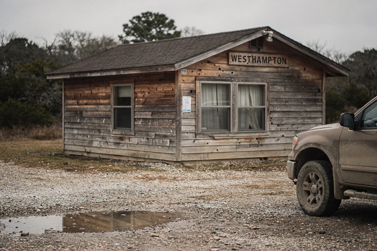 A small wood-sided trailhead office building with a gravel lot and a truck parked nearby