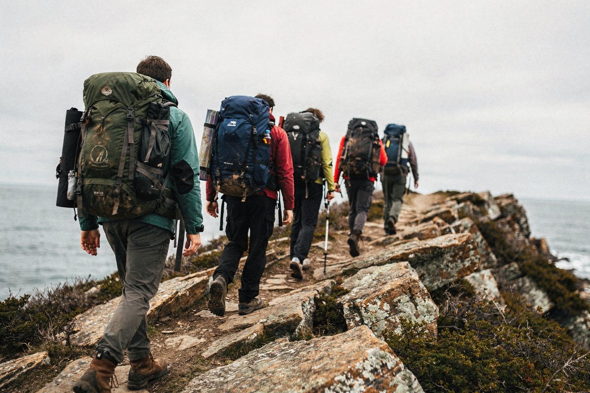 A line of hikers with full packs crosses an exposed rocky ridge under an overcast sky