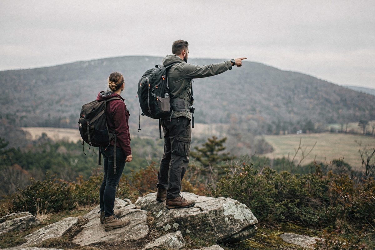 A guide points toward a distant ridge line from a summit rock outcrop