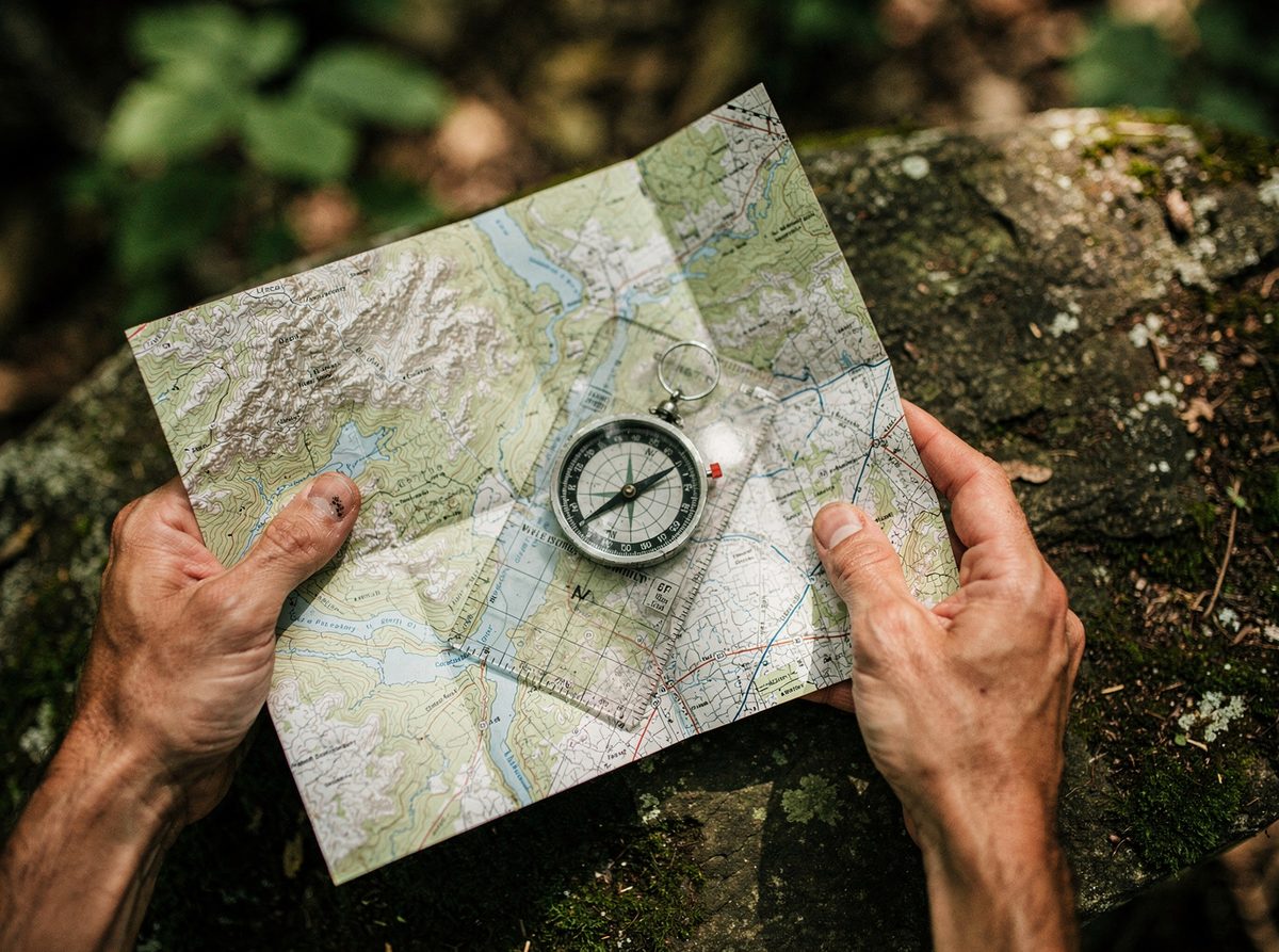 Hands hold a baseplate compass on a folded topographic map on a rock outdoors